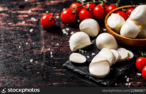 Sliced mozzarella on a stone board with tomatoes. Against a dark background. High quality photo. Sliced mozzarella on a stone board with tomatoes.