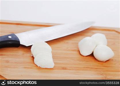Sliced mozzarella with knife on wooden board