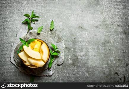 Sliced of ripe melon with branches of mint. On a stone background.. Sliced ripe melon with branches of mint.
