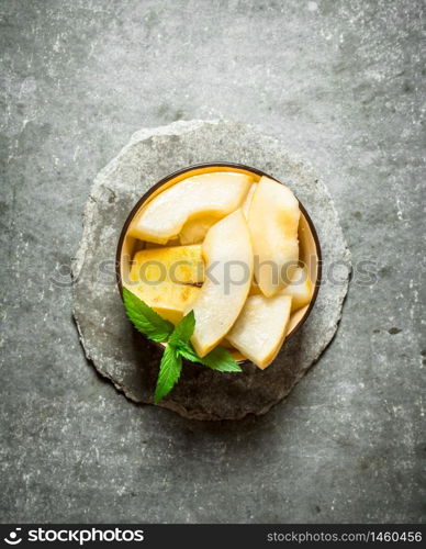 Sliced of ripe melon with branches of mint. On a stone background.. Sliced ripe melon with branches of mint.