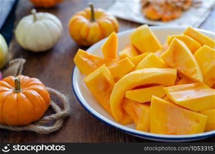 Sliced of the pumpkins in white enamel plate on wooden table.