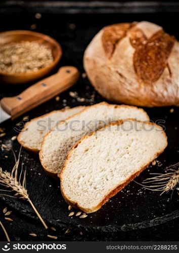 Sliced on a stone board wheat bread with grains. On a black background. High quality photo. Sliced on a stone board wheat bread with grains.