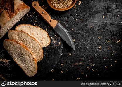 Sliced on a stone board wheat bread with grains. On a black background. High quality photo. Sliced on a stone board wheat bread with grains.