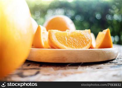 Sliced Orange on Wooden Plate. Fresh Juicy Fruit in Summer. Selective Focus. Blurred Tree with Lens Flare as background