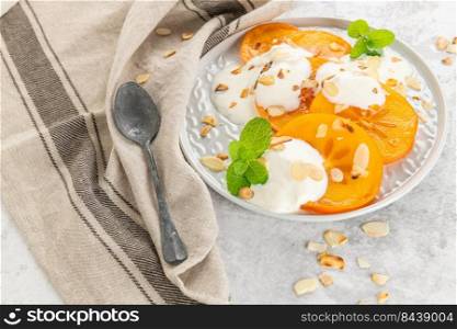 Sliced persimmon with yogurt and almonds. Healthy food concept on light background. top view