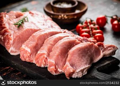 Sliced pork raw on a cutting board. On a rustic dark background. High quality photo. Sliced pork raw on a cutting board.