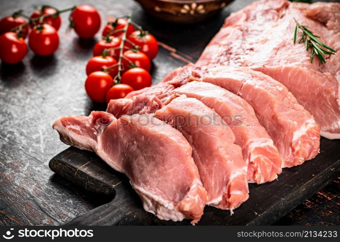 Sliced pork raw on a cutting board. On a rustic dark background. High quality photo. Sliced pork raw on a cutting board.