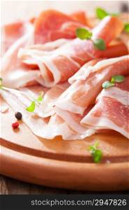 sliced prosciutto ham on chopping board with oregano and pepper