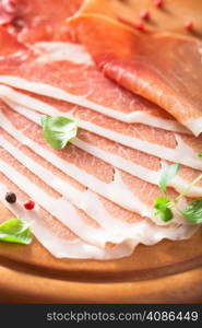 sliced prosciutto ham on chopping board with oregano and pepper