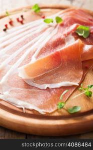 sliced prosciutto ham on chopping board with oregano and pepper