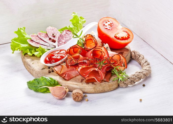 Sliced prosciutto with salami,cheese and basil on a wooden board