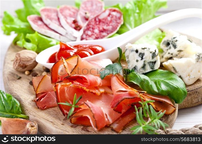 Sliced prosciutto with salami,cheese and basil on a wooden board