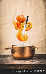 Sliced pumpkin with knife and cooking pot on wooden tables at wall background, pumpkin cooking preparation for autumn seasonal recipes and eating , front view. Flying food concept
