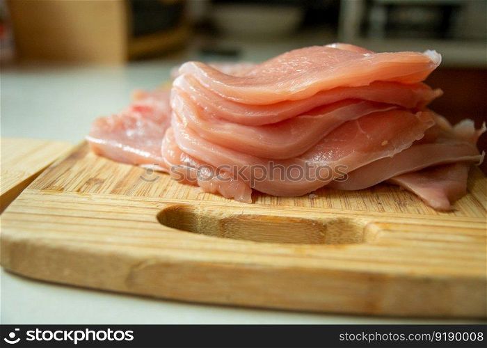 Sliced raw pork loin lying on a wooden board, close-up