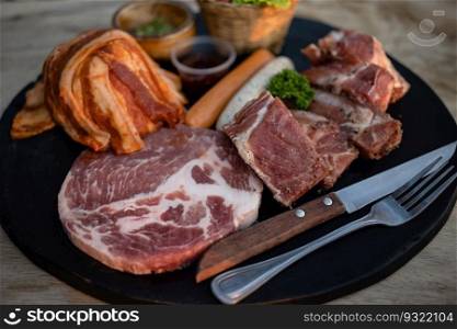 Sliced raw pork meat and sausage on black plate.