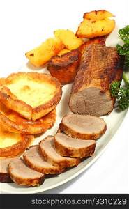 Sliced roast beef joint on a plate with Yorkshire puddings and roast potatoes, viewed from a high angle.