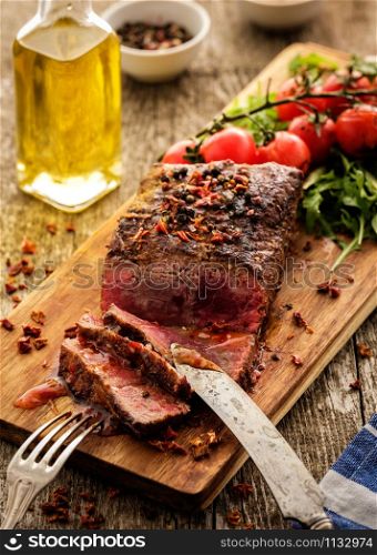 Sliced Roast beef on cutting board with grilled vegetables