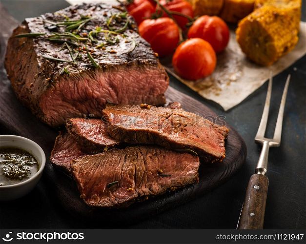 Sliced Roast beef on cutting board with grilled vegetables, close-up.