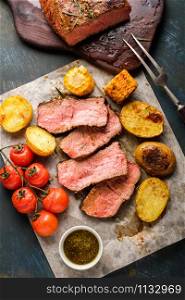 Sliced Roast beef on cutting board with grilled vegetables. View from above.