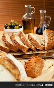 Sliced rustic bread and bread knife with olives, olive oil and balsamic vinegar