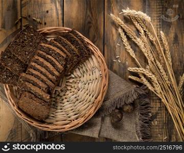 Sliced rye bread in a wicker tray and spikelets on wooden surface. loaf of bread top view