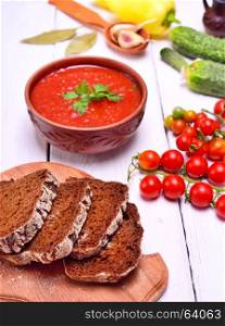 Sliced rye bread on a kitchen board, behind a tomato soup in a brown plate on a white table