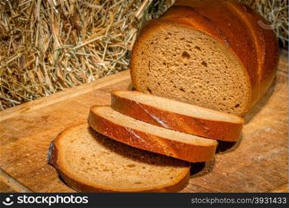 sliced rye bread on a wooden board near the haystack