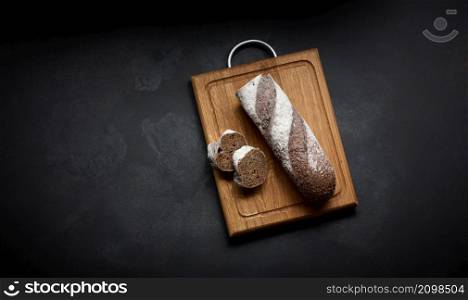 sliced rye flour baguette lies on a brown wooden board, top view