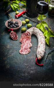 Sliced Salami stick with antipasti , red wine and grape leaves on dark vintage background. Italian food