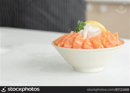 Sliced salmon sashimi laid out on ice in a white Japanese style bowl served with sliced lemon and radish. Japanese food home cooked concept