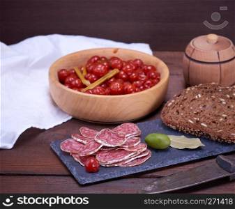 sliced smoked salami sausages and pieces of rye bread with sesame seeds on a black board