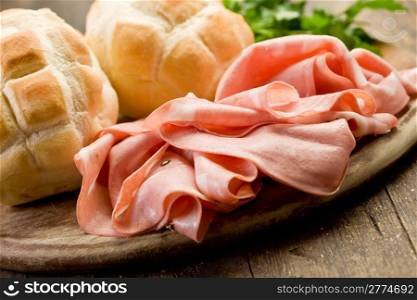 Sliced soft mortadella sausage on wooden table with bread