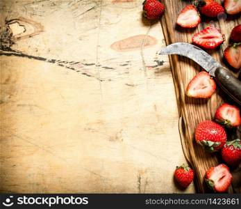 Sliced strawberries with the old knife on the Board. On wooden background.. Sliced strawberries with the old knife on the Board.