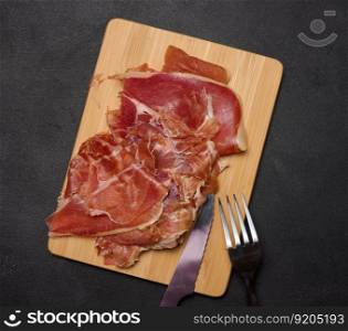 Sliced thin pieces of jamon on a wooden board, black table