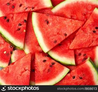 sliced triangular slices of ripe red watermelon with brown seeds, bright summer texture backdrop