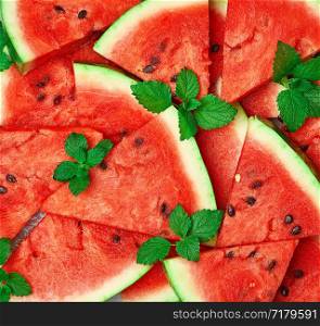 sliced triangular slices of ripe red watermelon with seeds with green mint leaves, bright summer texture backdrop