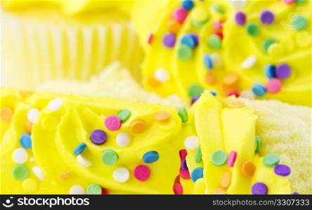 Sliced vanilla cupcakes with sunny yellow frosting are in front of whole cupcakes in selective focus macro; close up;