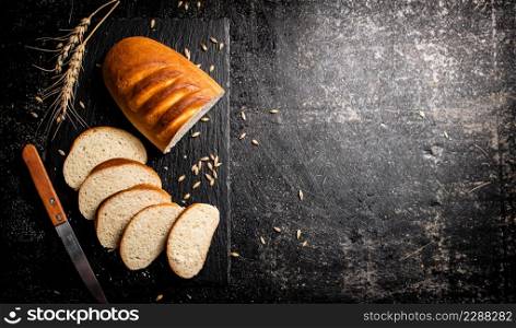 Sliced wheat bread with a knife on a stone board. On a black background. High quality photo. Sliced wheat bread with a knife on a stone board.