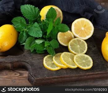 sliced yellow lemons on a brown wooden board, next to it lies a bunch of green mint, ingredients for making summer drinks