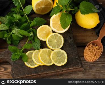 sliced yellow lemons on a brown wooden board, next to it lies a bunch of green mint, ingredients for making summer drinks