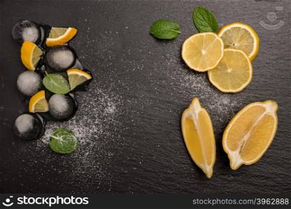 Slices and half fresh juicy lemon with mint leaves and melting ice on a slate board