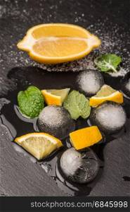 Slices and half fresh juicy lemon with mint leaves and melting ice on a slate board