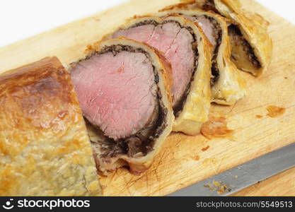 Slices from a beef wellington or boeur en crout on a wooden chopping board with a knife.