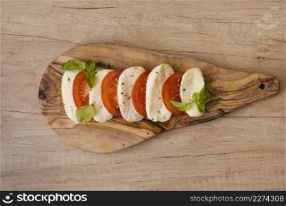 slices mozzarella cheese tomatoes with herb chopping board against wooden backdrop
