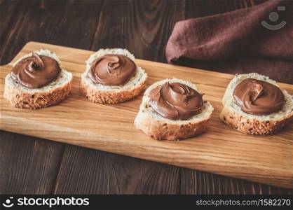 Slices of baguette with chocolate paste on wooden board