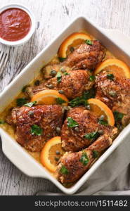 Slices of baked chicken in a creamy sauce with oranges and capers in a baking dish