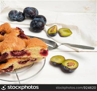 slices of biscuit plum cake on a white wooden board and fresh fruits, close up