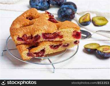 slices of biscuit plum cake on a white wooden board and fresh fruits, top view
