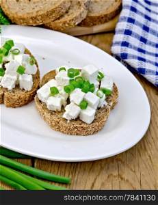 Slices of bread with feta cheese and chives on a plate, napkin on the background of wooden boards