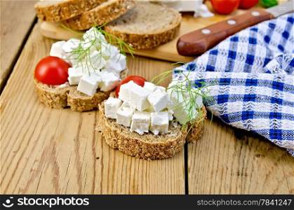 Slices of bread with feta cheese, tomato and dill, a napkin on a wooden boards background